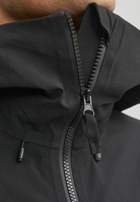 Schwarze wasserdichte Jacke mit hohem Kragen, ausgestattet mit einem zentralen Reißverschluss und Taschenverstellern. Glatte Textur ohne sichtbare Muster.