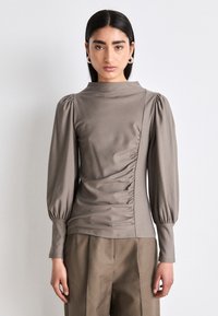 Haut à manches longues et col montant en tissu taupe avec détail froncé sur les côtés et manches volumineuses. Assorti à un pantalon large taille haute.