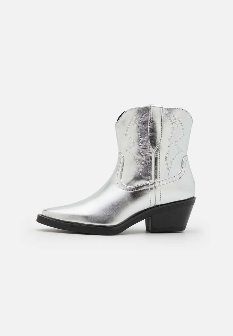 Botas de vaquero de cuero plateado con puntera afilada, detalles bordados en el eje y un tacón negro moderado. Superficie lisa y brillante.