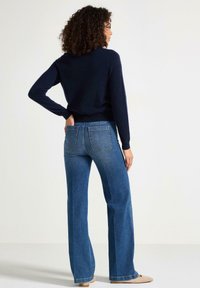 Maglione blu scuro e jeans a campana blu chiaro. I jeans presentano tasche posteriori e una vestibilità dritta, mentre il maglione ha maniche lunghe.