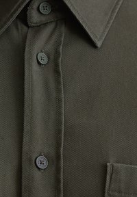 Camicia button-up verde scuro con dettaglio ravvicinato sul colletto, bottoni e cuciture della tasca sul petto.