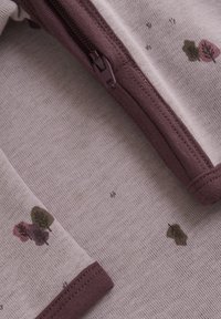 Ljuslila zip-up jacka med blommönster i djup lila och grön. Slät tyg, ribbade muddar och dragkedjedetalj.