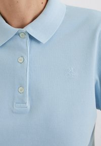 Lichtblauw polo shirt van een textuurstof, met een drie-knopen sluiting en een klein geborduurd logo op de borst.