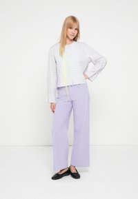 Grå ternet cropped jakke med gule bånd, kombineret med lys lilla bukser med vide ben. Sorte flade sko fuldender outfittet.