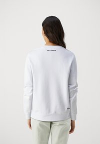 Hvit genser med lange ermer, med rund hals og en logo trykket i svart på baksiden. Ribbestrikkede mansjetter og søm. Casual passform.