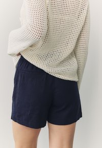Navy blue linen shorts with a relaxed fit and side pockets, paired with a loose-knit cream sweater featuring a textured weave.