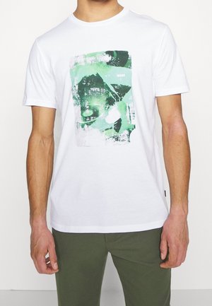 White cotton t-shirt featuring a green abstract graphic print at the chest. Round neck, short sleeves, and regular fit design.