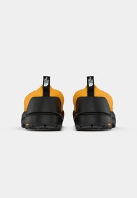 Chaussures de randonnée jaunes et noires avec une tige rembourrée, une semelle robuste et des languettes de tirage proéminentes. Présente un matériau durable et une surface texturée.