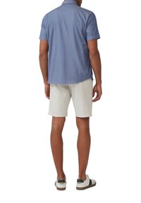 Jasnoniebieska koszula z krótkim rękawem i wyłogami, zestawiona z kremowymi szortami i białymi trampkami z czarnymi akcentami.