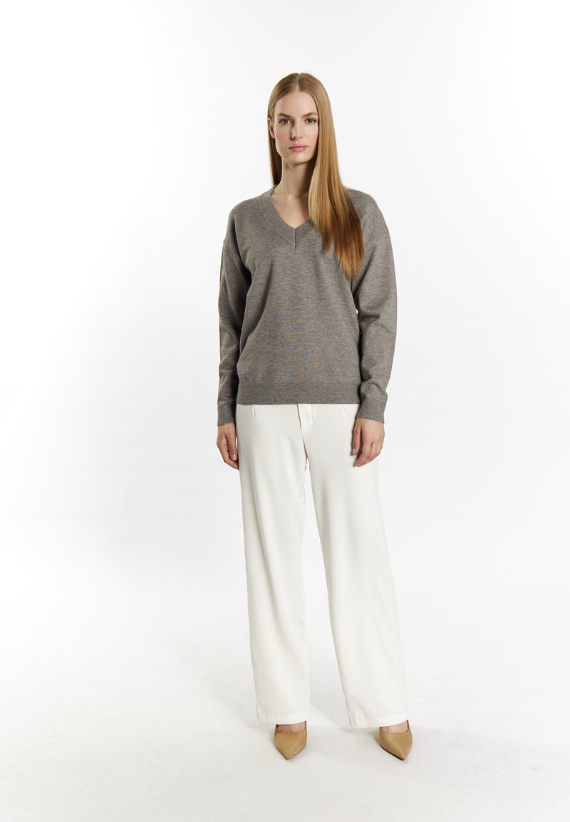 Hellgrauer V-Ausschnitt-Pullover mit gerippten Bündchen, kombiniert mit weißen, weit geschnittenen Hosen und beigen spitz zulaufenden High Heels. Minimalistisches Design, glatte Textur.