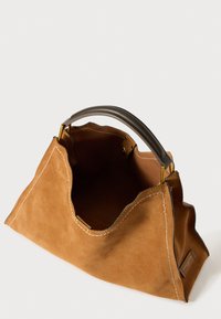 Ruskea nubukista valmistettu käsilaukku, jossa on pehmeä, kaareva muoto, tummat kontrastivärit käsikahvassa ja näkyvissä olevat ompeleet. Avoin yläosa paljastaa tilavan sisätilan.