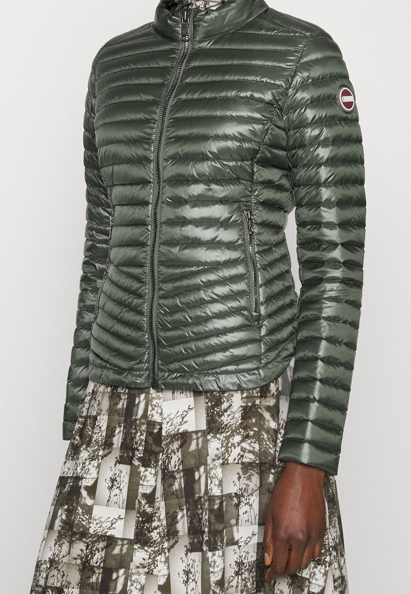 Zelená prošívaná péřová bunda na zip vpředu, s vysokým límcem. Dvě boční kapsy s elegantním lesklým povrchem.