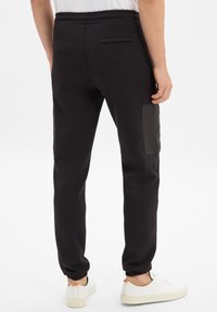 Zwarte joggingbroek met een elastische tailleband, zij- en achterzakken, en een soepele textuur. Gedetailleerd met een paneel op één bovenbeen en geribbelde boorden.