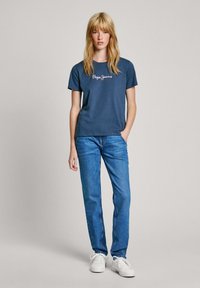 Marinblå bomullströja med vitt "Pepe Jeans"-logga, ihop med jeans i medelblå tvätt och vita snörskor.