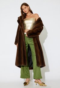 Bruine nepbontjas over een gouden strapless crop top, gecombineerd met groene wijde pantalons en metallic gouden slingbackhakken.