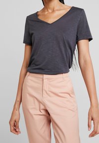 Grå V-ringad T-shirt gjord av lätt tyg med korta ärmar, kombinerad med ljusrosa skräddarsydda byxor. Har en avslappnad passform.