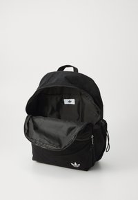 Rucsac din material textil negru, cu exterior texturat, închidere cu fermoar și un compartiment principal. Prezintă un accent de logo alb în față.