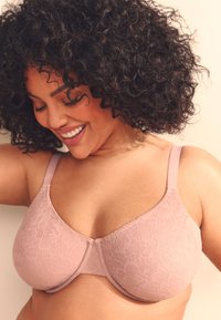 Soutien-gorge en dentelle rose clair avec une finition lisse, doté de bretelles ajustables et d'un motif floral subtil sur les bonnets.