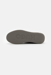 Grå såle med teksturert overflate, med innfelt "HUGO" branding. Flat design og glatte kanter for komfort og støtte.