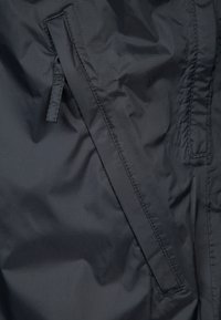 Chaqueta de nylon negra con un bolsillo lateral con cremallera, textura suave y un brillo sutil. El detalle de costura realza el diseño estructurado.