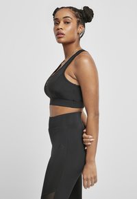 Čierny športový crop top a legíny s vysokým pásom, vyrobené z hladkej tkaniny; obsahujú sieťované panely, akcenty s logom a priliehavý strih.