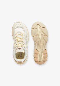Baskets Lacoste en cuir crème, avec un dessus texturé, des accents beige clair, une épaisse semelle en caoutchouc avec un motif en zigzag et un détail de logo.