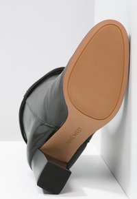 Bota de cuero negro con acabado texturizado, tacón cuadrado y suela de goma con patrón de agarre segmentado. Nombre de la marca estampado en la suela.