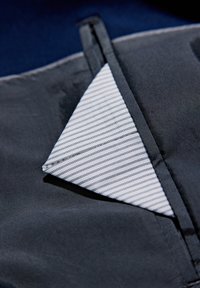 Tejido gris oscuro con un bolsillo que presenta un forro interior a rayas blanco y marino. Textura suave, costuras precisas y forma triangular.