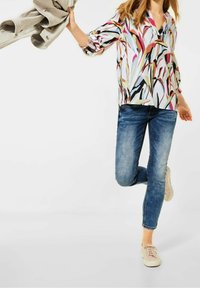 Blouse à motif floral avec un col en V et des manches froncées, associée à un jean skinny bleu et des baskets rose clair.