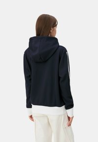 Felpa navy con una grande cappuccio, dettagli bianchi su polsini e orlo, e design aderente. Tessuto liscio e estetica semplice e moderna nella vista posteriore.