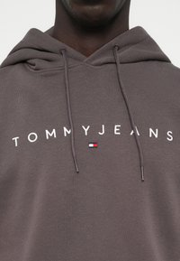 Hanorac gri din amestec de bumbac, cu glugă ajustabilă, inscripționat cu textul brodat alb "TOMMYJEANS" și un logo mic în roșu, alb și albastru.