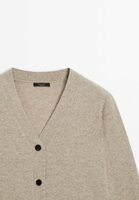 Cardigan gris clair en tissu tricoté doux et texturé. Doté d'un col en V et de deux boutons noirs à l'avant. Design simple et polyvalent.