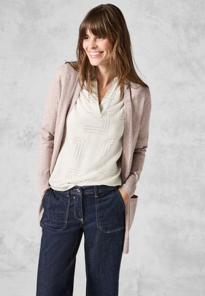 Light pink cardigan over a cream blouse with geometric patterns and dark denim wide-leg trousers. Smooth textures, casual fit.
