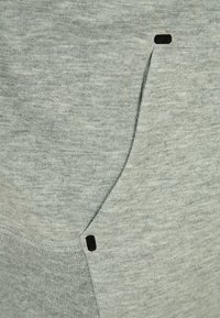 Grijze sweatshirstof met een zachte textuur, voorzien van een zijzak met zwarte accenten en stiksels. Eenvoudig ontwerp, zonder patronen.