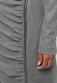 Vestido de tecido cinza com um design com folhos ao longo do lado esquerdo e um detalhe de fecho prata. O material parece suave, com um acabamento texturizado.