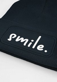 Knit navy beanie with ribbed texture, featuring a rectangular patch with the word "smile." in white, prominently displayed on the front.