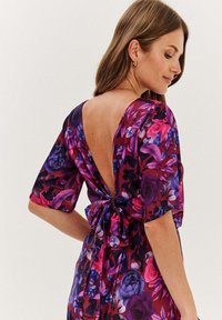 Kwiatowa sukienka w intensywnych kolorach purpury, różu i czerni. Płynący materiał z głębokim dekoltem w kształcie V i kokardą w talii. Krótkie rękawy.