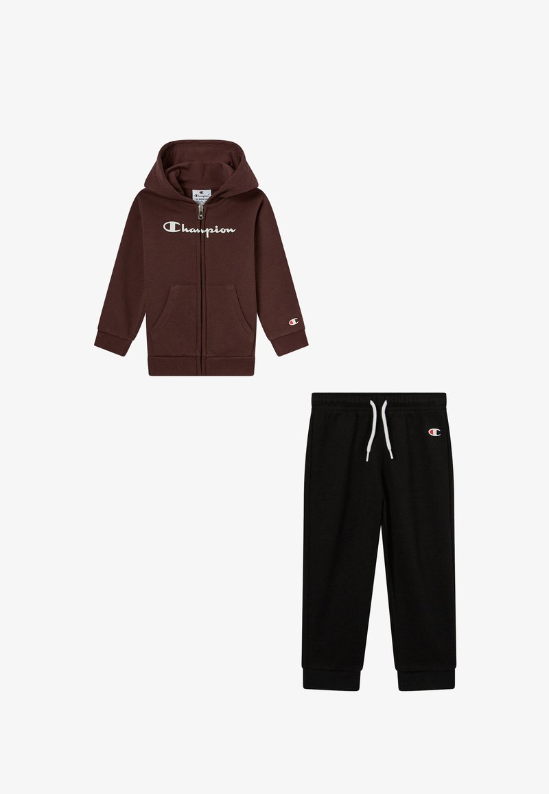 Sudadera marrón con cremallera y bolsillos frontales, y logo blanco; pantalones de chándal negros con cintura elástica y cordón. Ambos son de tejido suave.