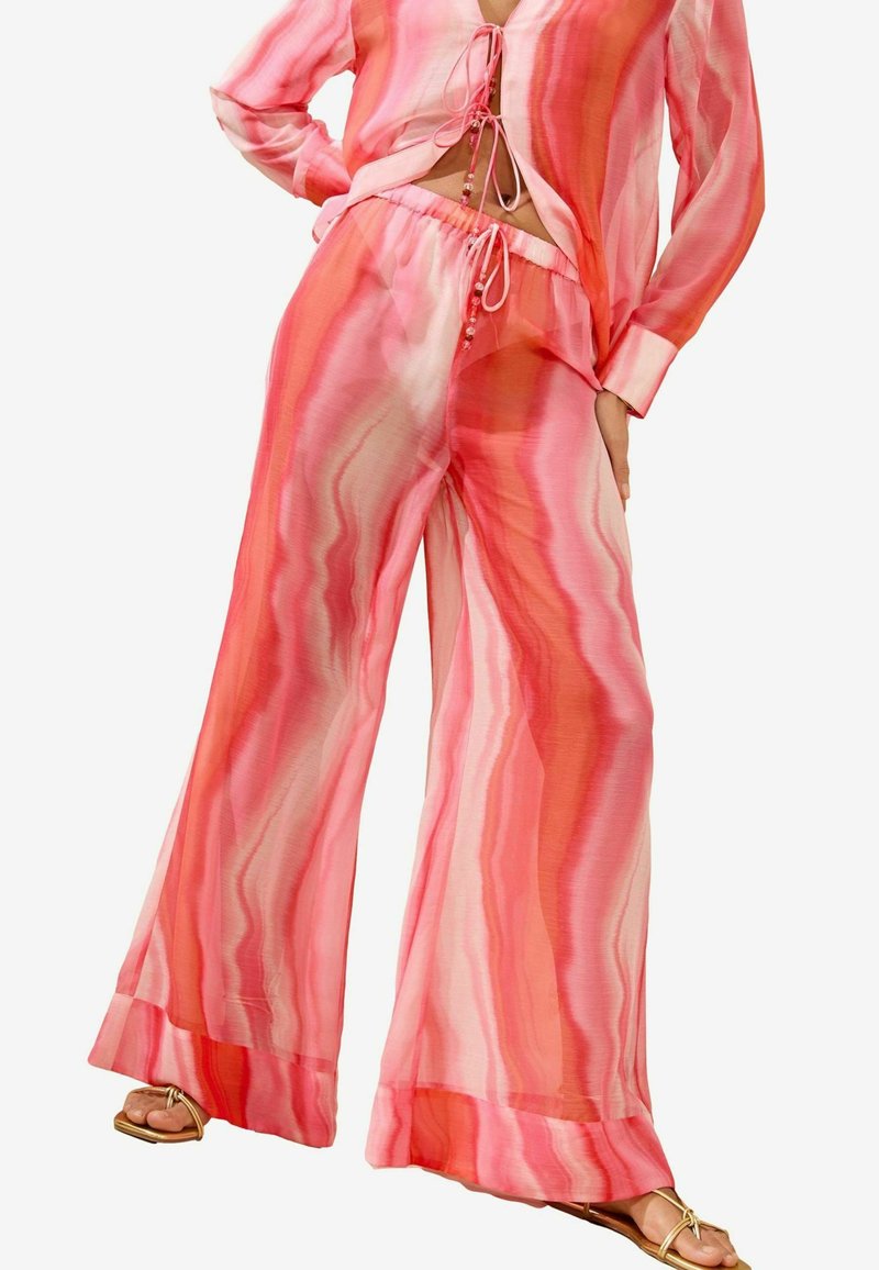 Zwei-teiliger Anzug aus leichtem, transparenter Stoff. Das Oberteil ist pink mit gewellten Mustern und Schlaufenbändern; die Hose ist ausgestellt und passt mit einem ähnlichen Design dazu.