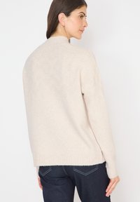 Beige pletený svetr s pružným lemem, s vysokým límcem a jemným texturovaným vzorem, spárovaný s tmavě modrými džíny.