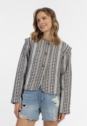 Giacca tessuta con un design a fantasia in navy, bianco e oro, caratterizzata da un collo arrotondato e tre bottoni frontali, abbinata a pantaloni corti in denim sfilacciati.