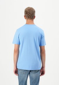 Világoskék, rövid ujjú póló, kerek nyakkivágással, pamutból készült. Simma textúrája van. Világoskék farmerral viselve.