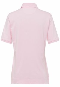 Polo en tissu rose doux, doté d'un col classique, de manches courtes et d'une texture lisse. Aucun motif ni élément métallique visible.