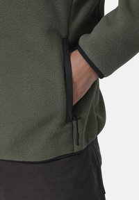 Fleecejacke in Dunkelgrün mit strukturierter Oberfläche, ausgestattet mit einer seitlichen Reißverschlusstasche und schwarzem Besatz an den Bündchen und dem Saum.