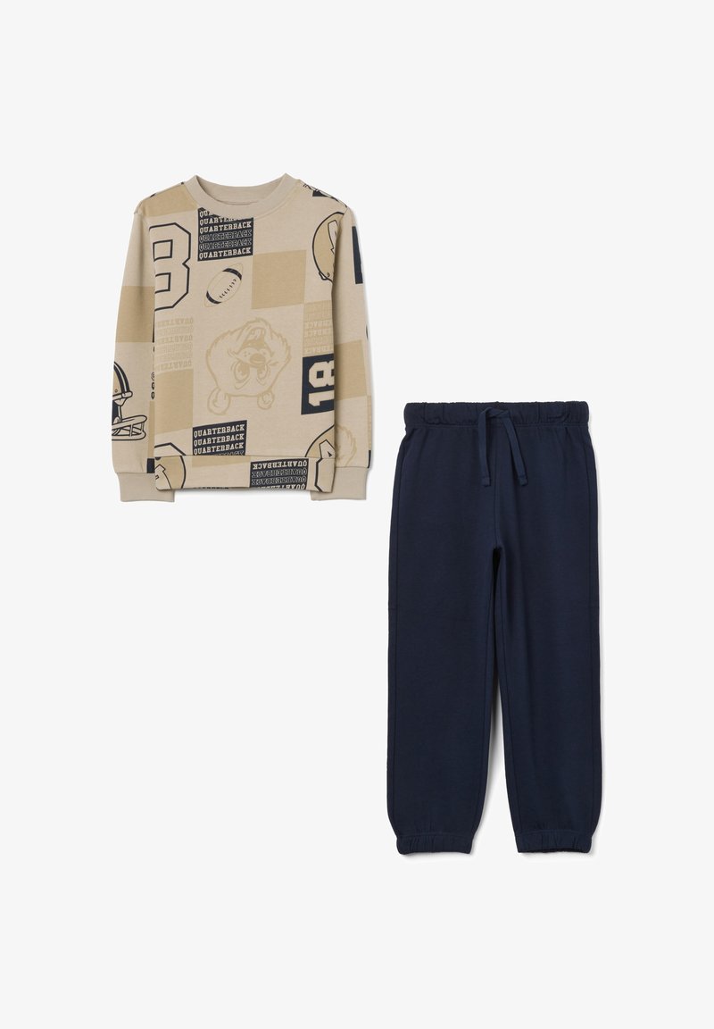 Felpa beige a motivi con pantaloni jogging blu navy. La felpa presenta grafiche e testi a tema sportivo; i pantaloni hanno una vita elasticizzata e polsini.