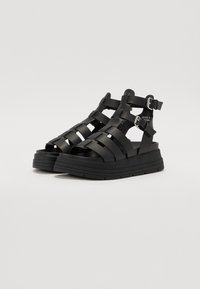 Sandale platform din plastic modelat, de culoare neagră, cu un design de curea țesută și cataramă ajustabilă. Talpă groasă, texturată pentru aderență.