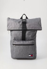 Gray fabric backpack with a roll-top closure, black strap, front zip pocket, and logo patch. Textured surface with a heathered pattern.