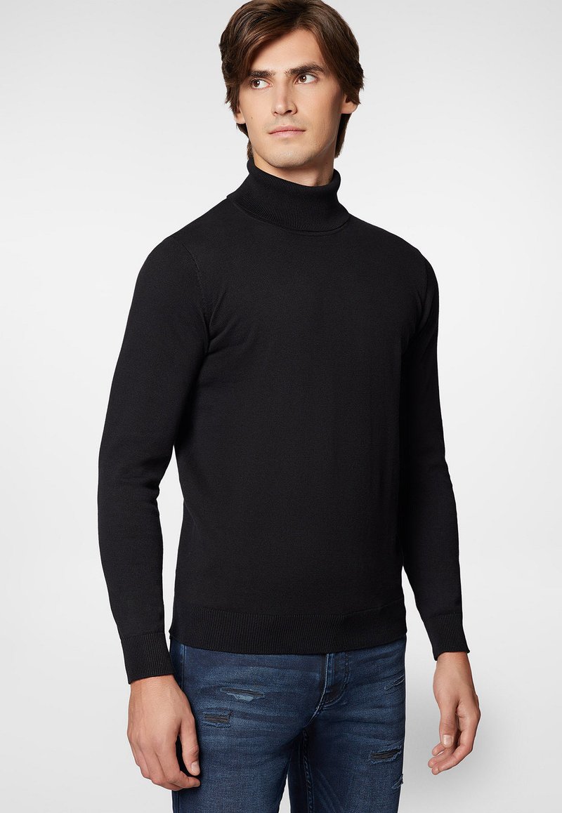 Czarny sweter z golfem wykonany z materiału prążkowanego, z długimi rękawami i dopasowanym krojem, w połączeniu z zniszczonymi niebieskimi dżinsami.