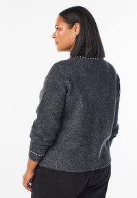 Siva pletena majica s udobnim krojem; ima biserne detalje duž stražnjeg izreza i rebraste manžete. Mekana tekstura i srednja težina.