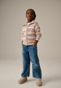 Mehrfarbiger gestreifter Strick-Zipfel-Pullover mit gerippten Kanten, kombiniert mit lockeren, ausgebleichten blauen Jeans und beigefarbenen Slippern.